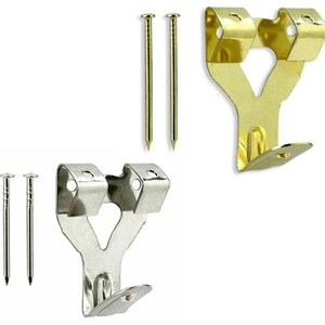 May include: Two gold-coloured picture hangers and two silver-coloured picture hangers are displayed, each with two small nails. The hangers have a hook shape for hanging pictures. The nails are thin and have a pointed end.