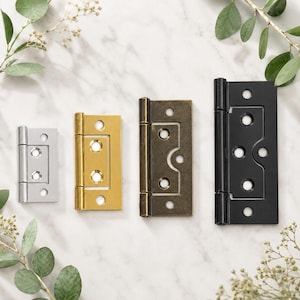 May include: Four rectangular metal hinges arranged in a row, varying in size and finish. The hinges are silver, polished gold, antique brass, and matte black. Each hinge features a central pin and multiple circular screw holes for mounting.