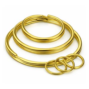 May include: Several gold-coloured key rings of different sizes. The key rings are arranged in a layered composition, with larger rings behind and smaller rings in front. The rings have a smooth, shiny finish.