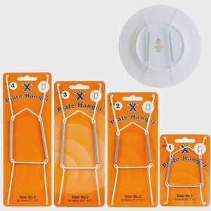 May include: Four plate hangers on orange cards, with white wire frames and silver springs. Sizes range from 13-41cm (5"-16"). A white plate with a gold emblem is shown with a hanger attached. The text "Plate Hanger" is visible on the cards.