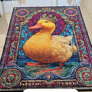 May include: A decorative rug featuring a yellow duck wearing a crown, set against a stained-glass style background. The duck stands in water, with a vibrant color palette of blues, pinks, and golds. The word "Sample" is printed on the rug.