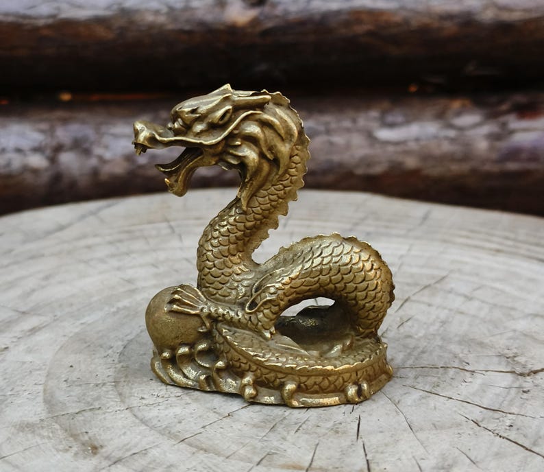 May include: A detailed brass dragon figurine with an open mouth and intricate scale details. The dragon is posed on a round base, with a ball held in its claw. The figurine is approximately 4 inches tall.