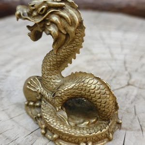 May include: A detailed brass dragon figurine with an open mouth and scaled body. The dragon is posed in a curved position, with its head raised. The figurine is on a small base and has a golden color.