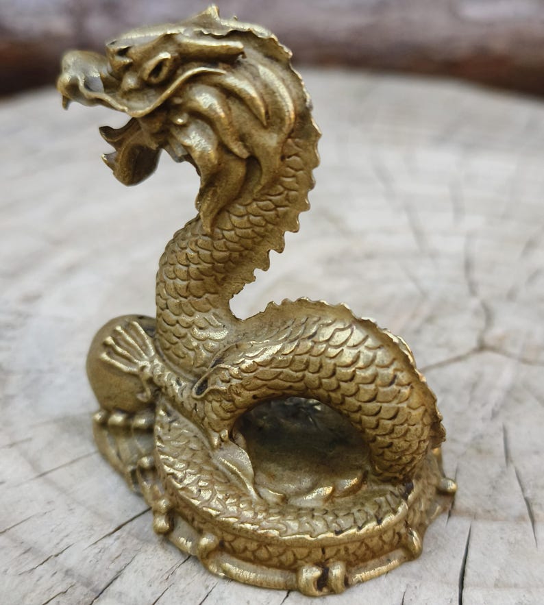 May include: A detailed brass dragon figurine with an open mouth and scaled body. The dragon is posed in a curved position, with its head raised. The figurine is on a small base and has a golden color.