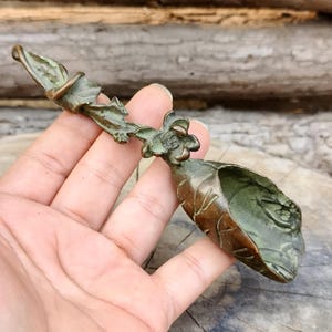 May include: A bronze scoop with a floral and leaf design. The scoop features a long handle with a flower and a leaf-shaped bowl. This decorative piece could be a serving utensil or a unique kitchen item.