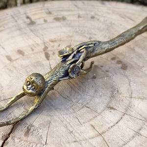 May include: A bronze-colored bottle opener in the shape of a monkey clinging to a branch. The monkey has outstretched arms and a detailed face. The branch features floral accents and a curved handle.