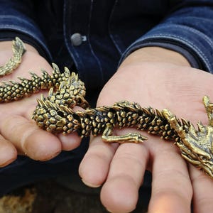 May include: Detailed brass dragon figurine with textured scales and intricate details. The dragon is posed in a curved position, with its head and tail visible. The dragon is a golden color.