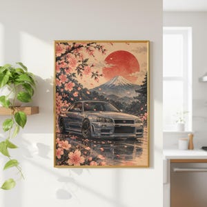 Puede incluir: Una impresión de arte mural enmarcada que muestra un coche deportivo plateado aparcado sobre una superficie mojada, rodeado de ramas de cerezo en flor rosas. Al fondo, un gran sol rojo sale tras una montaña nevada, creando una composición.