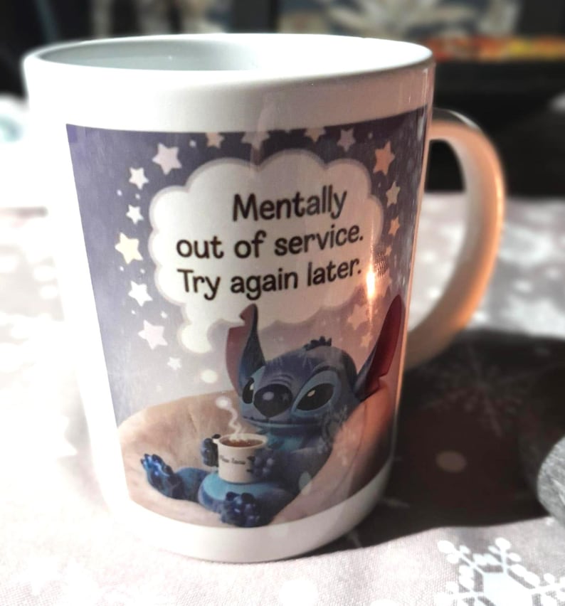 Pu&ograve; includere: Tazza in ceramica bianca con un'immagine a cartoni animati di Stitch di Lilo & Stitch, che tiene una tazza di caff&egrave;. La tazza ha il testo "Mentally out of service. Try again later" in un fumetto con stelle.