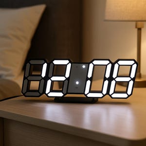 Può includere: Un moderno orologio digitale che mostra "02:08" con luci LED bianche brillanti. L'orologio ha una cornice nera e si trova su un comodino di legno. Una lampada con un paralume beige è sullo sfondo, creando un'atmosfera calda.