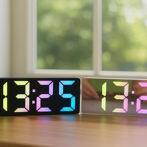 Peut inclure: Deux réveils numériques affichant l'heure 13h25. L'un est noir, l'autre argenté avec une face miroir. Les chiffres sont éclairés d'un dégradé arc-en-ciel de couleurs, dont le jaune, le rose et le bleu.