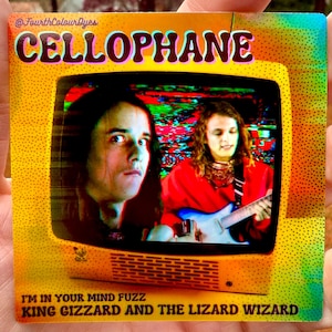 May include: A square sticker with a yellow border and the word "CELLOPHANE" in large, colorful letters. The sticker features a retro television screen displaying two people, one playing a guitar. The text "I'M IN YOUR MIND FUZZ" and "KING GIZZARD AND THE LIZARD WIZARD" are also visible.
