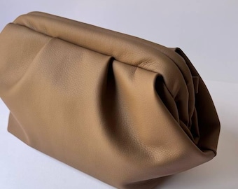 Puede incluir: Un bolso de mano de color marrón claro con un diseño suave y fruncido. El bolso está hecho de un material liso y tiene forma rectangular con bordes redondeados. La parte superior del bolso está fruncida, creando un efecto texturizado.
