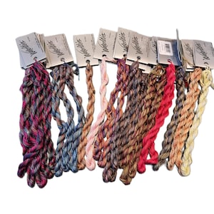 May include: A collection of ten skeins of Waterlilies embroidery thread, each attached to a branded paper tag. The threads feature variegated colour palettes including shades of pink, blue, brown, red, and yellow, presented in twisted strands.
