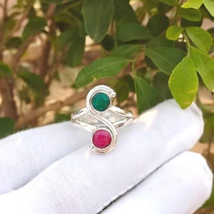 Puede incluir: Anillo de plata con un diseño único, con dos piedras redondas. Una es verde vibrante, la otra roja intensa. El diseño del anillo tiene una forma fluida y elegante, ideal para cualquier ocasión.