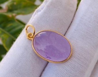 May include: A gold pendant with an oval, light purple gemstone. The gemstone is set in a gold bezel and has a smooth, polished surface. The pendant has a small gold loop for a chain.