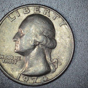 May include: A close-up of a United States quarter coin. The coin features a profile of George Washington, the word "LIBERTY" at the top, and "IN GOD WE TRUST" below. The year "1974" is visible at the bottom. The coin is silver in color.