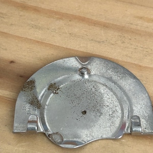 May include: A semi-circular silver-toned metal component featuring a central hole, two small tabs at the base, and a raised stud. The surface shows signs of wear and oxidation. Embossed text on the left side reads 32622 SIMA USA.