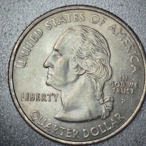 May include: A close-up of a United States quarter coin. The coin features a profile of George Washington, the words "LIBERTY", "QUARTER DOLLAR", and "IN GOD WE TRUST". The coin is silver in color.