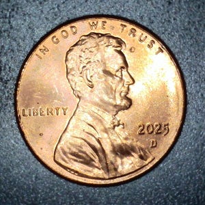 May include: A copper-colored United States penny coin, featuring the profile of Abraham Lincoln. The coin displays the year 2025 and the inscriptions "IN GOD WE TRUST" and "LIBERTY".