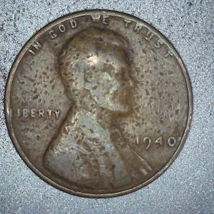 May include: A close-up of a 1940 United States penny. The coin features the profile of a person, the word "LIBERTY", and the phrase "IN GOD WE TRUST". The year "1940" is visible. The coin has a worn, aged appearance.