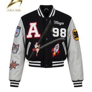May include: A black and light gray varsity jacket featuring a large red letter A, the name Maya, and the number 98. The jacket includes various embroidered patches, including a rocket, a cat, and a pin-up style figure on the front and sleeves.