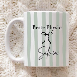 Könnte beinhalten: Weiße Keramik-Tasse mit hellgrünem Streifenmuster. Die Tasse zeigt den Text "Beste Physio" über einer schwarzen Schleifengrafik mit dem Namen "Silvia" in Schreibschrift darunter. Die Tasse hat einen weißen Henkel.