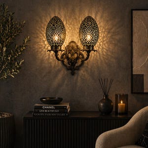 May include: A decorative wall sconce with two ornate, egg-shaped lampshades. The lampshades have a detailed, openwork design, casting intricate light patterns. The fixture is made of dark metal with a decorative central element, adding a touch of vintage elegance to the interior.
