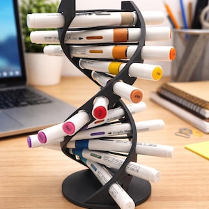 May include: A black plastic desk organizer shaped like a double helix DNA strand, featuring multiple horizontal slots holding various white acrylic markers with colored caps in shades of orange, yellow, red, pink, purple, and blue.