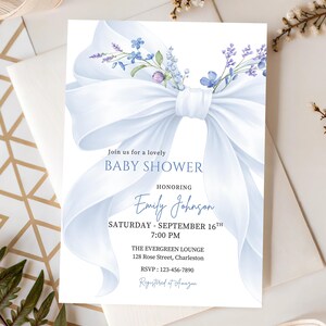 Può includere: Invito per baby shower con un grande fiocco azzurro e decorazioni floreali. L'invito include il testo "Join us for a lovely BABY SHOWER" e i dettagli del baby shower di Emily Johnson.