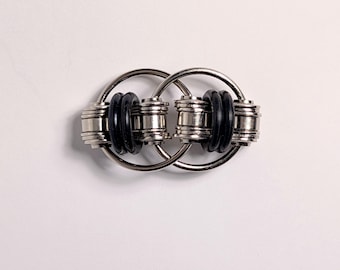 May include: A silver metal fidget toy with two interlocking rings. Each ring has two cylindrical silver beads and two black rubber rings. The toy is designed to be manipulated with the fingers.