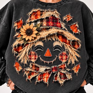 Op de afbeelding: Een antracietgrijs sweatshirt met een distressed-stijl afbeelding van een vogelverschrikkergezicht. Het ontwerp bevat gerafelde stoffen patches in rood en oranje ruitpatroon, een gele zonnebloem en een lachende vogelverschrikker met een driehoekige neus.
