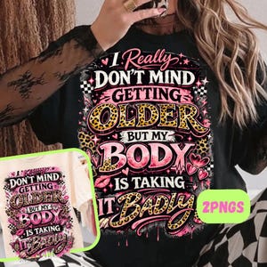 May include: Black t-shirt with a graphic design that reads "I Really Don't Mind Getting Older But My Body Is Taking It Badly." The design features pink, leopard print, and black accents. A second, similar shirt is also visible.