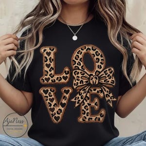 May include: Black t-shirt featuring the word "LOVE" in a leopard print design. The letters "L" and "E" have heart cutouts, and the "O" is a bow. A casual style top.