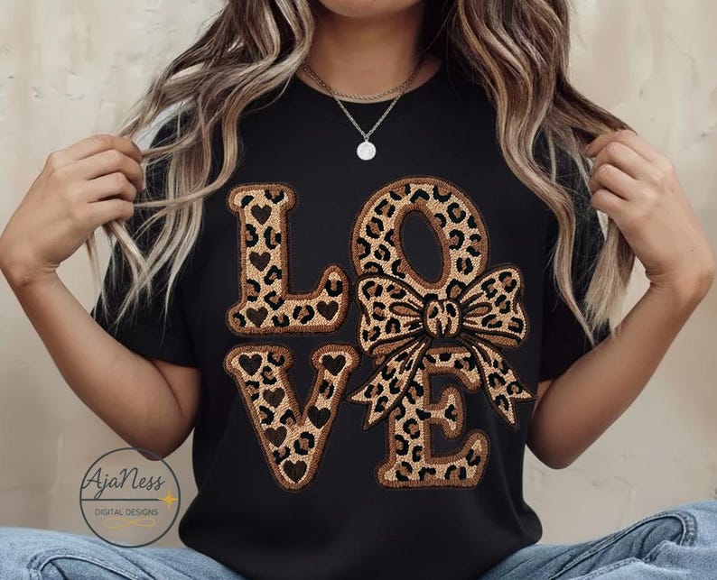 May include: Black t-shirt featuring the word "LOVE" in a leopard print design. The letters "L" and "E" have heart cutouts, and the "O" is a bow. A casual style top.