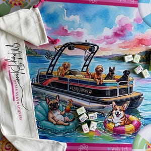 May include: A rectangular game mat featuring a watercolor illustration of dogs on a pontoon boat labeled Lake Days, with a French bulldog and a Corgi floating in the water. Includes a white drawstring bag with the text Mahj Bloom DESIGNSBYDAPHNED.