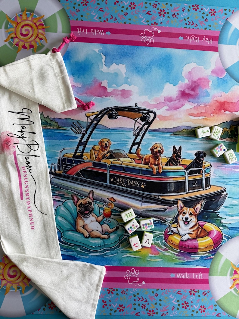 May include: A rectangular game mat featuring a watercolor illustration of dogs on a pontoon boat labeled Lake Days, with a French bulldog and a Corgi floating in the water. Includes a white drawstring bag with the text Mahj Bloom DESIGNSBYDAPHNED.