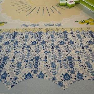 Puede incluir: Un juego de Mahjong sobre un tapete estampado. El tapete presenta un dise&ntilde;o de sol y patrones florales en azul y blanco. Las fichas verdes y blancas est&aacute;n apiladas sobre el tapete. El texto en el tapete dice "Play Right Walls Left" y "Charleston 2 - Right".