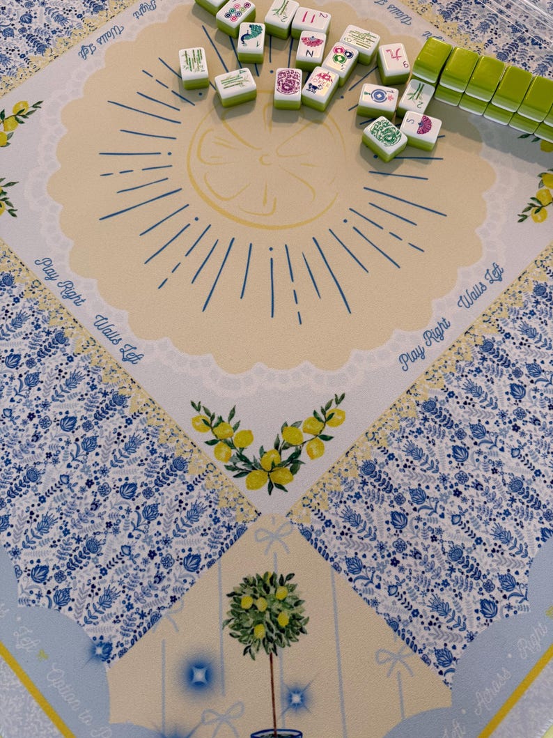Puede incluir: Un juego de Mahjong con un dise&ntilde;o de tem&aacute;tica de lim&oacute;n. El tablero presenta un centro amarillo con una ilustraci&oacute;n de rodaja de lim&oacute;n y bordes con motivos florales azules. Las fichas verdes y blancas est&aacute;n esparcidas por el tablero.
