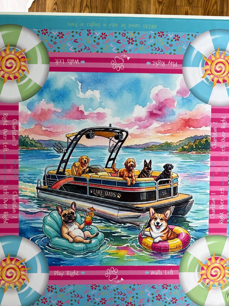 May include: A rectangular game mat featuring a watercolor illustration of a pontoon boat labeled Lake Days with several dogs on board. A French Bulldog and a Corgi float in the water. The border includes sun icons and text like Play Right.