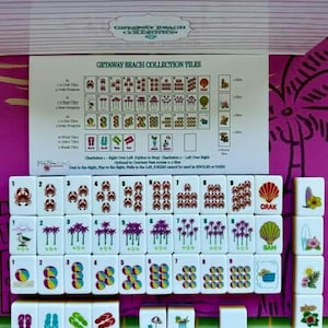 May include: A set of white Mahjong tiles from the Getaway Beach Collection, featuring colorful illustrations of crabs, palm trees, beach balls, and flip-flops. An instructional card displays the tile values and game rules for this themed set.