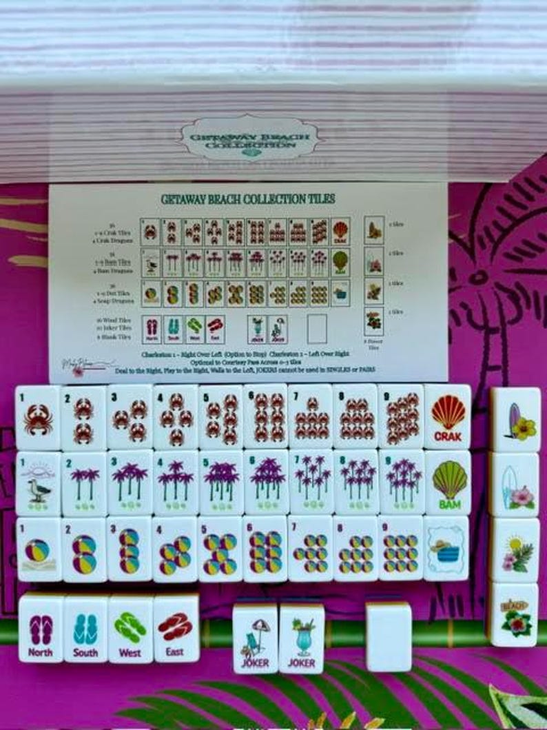 May include: A set of white Mahjong tiles from the Getaway Beach Collection, featuring colorful illustrations of crabs, palm trees, beach balls, and flip-flops. An instructional card displays the tile values and game rules for this themed set.