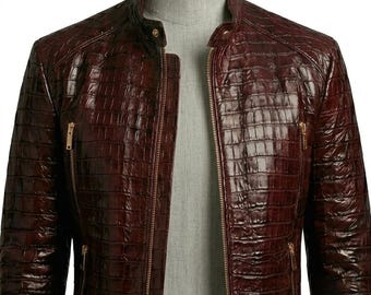 May include: A dark burgundy jacket with a glossy, textured finish resembling crocodile skin. The jacket features a stand-up collar with a snap button, a full-length front zipper, and two vertical zippered pockets on the chest with gold-toned hardware.