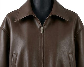 May include: A dark brown jacket with a smooth finish, featuring a wide collar, long sleeves, and a central metal zipper closure. The garment includes two vertical slit pockets on the front, providing a clean and structured appearance.
