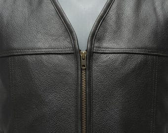 May include: A black leather vest featuring a textured grain surface, a deep V-neckline, and a central vertical zipper closure with a metallic pull. The garment includes horizontal seam detailing across the chest and vertical seams along the front.