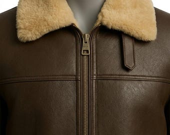 May include: A dark brown jacket featuring a tan faux shearling collar, a central metal zipper closure, and horizontal seam detailing across the chest. The garment includes a small vertical tab detail near the collar and a smooth texture.