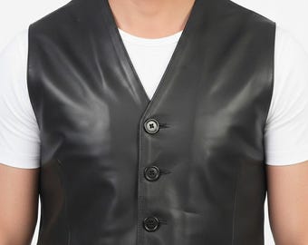May include: Black leather vest with a V-neck design and three button closure. The vest has a textured surface and a tailored fit. The vest is worn over a white t-shirt.