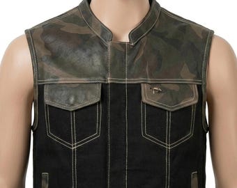 May include: A sleeveless vest featuring a camouflage pattern on the upper chest and shoulders, contrasted with a solid black lower section. The garment includes two chest pockets with flaps, light-colored stitching, and a small metallic emblem.