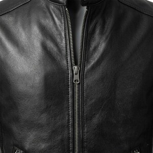 Puede incluir: Una chaqueta negra con una superficie lisa y texturizada y una cremallera metálica vertical central. La prenda incluye un cuello alzado y costuras visibles a lo largo de los paneles frontales, mostrando un diseño limpio, estructurado y con herrajes metálicos.