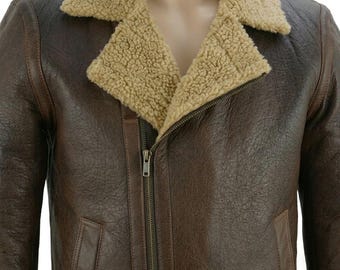 May include: A dark brown leather jacket featuring a textured finish, a tan faux-shearling collar, and an off-center metal zipper closure. The garment includes two side pockets and long sleeves, providing a structured look with a warm lining.
